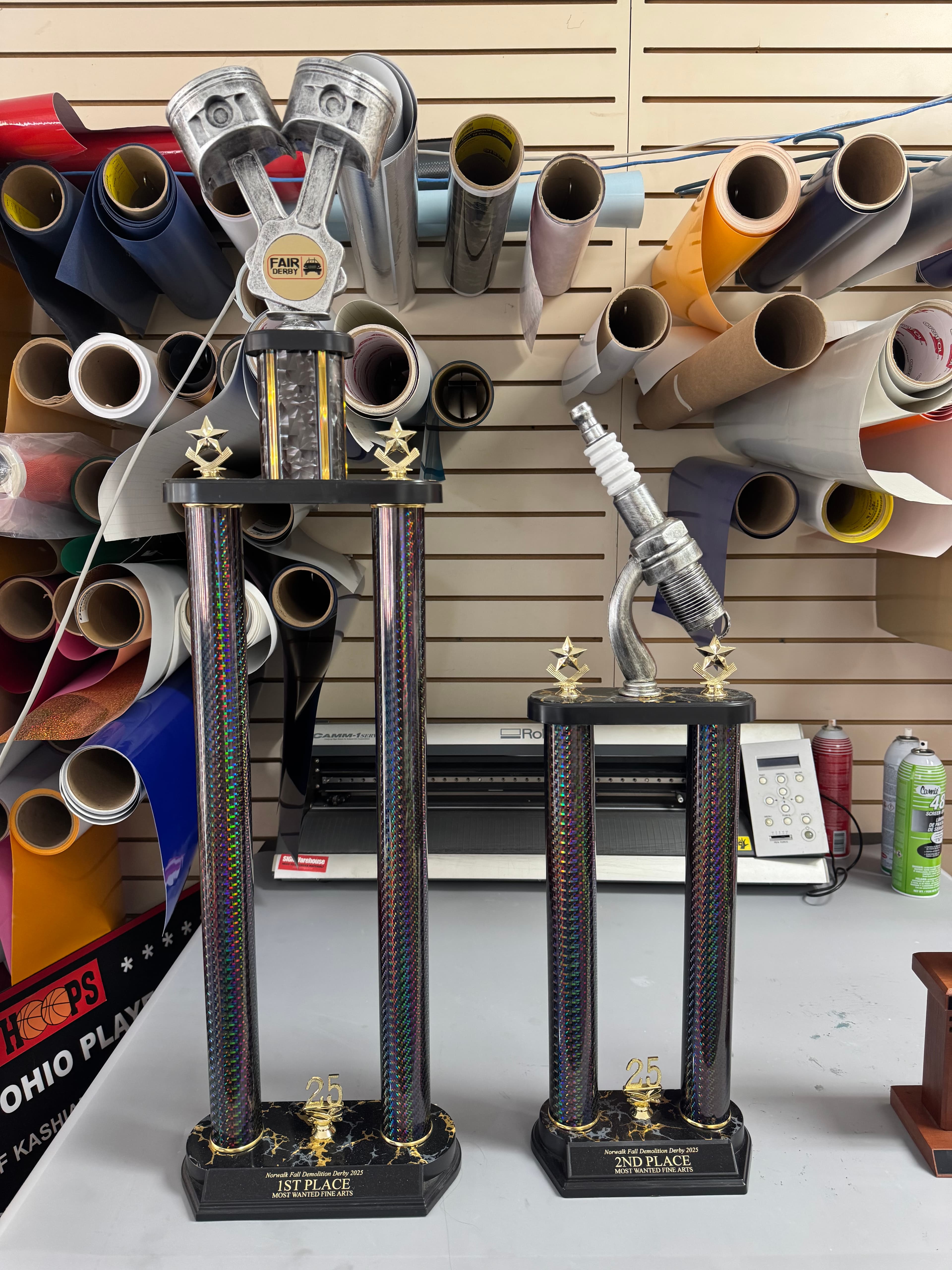 Tall first and second place demolition derby trophies with piston and spark plug toppers.