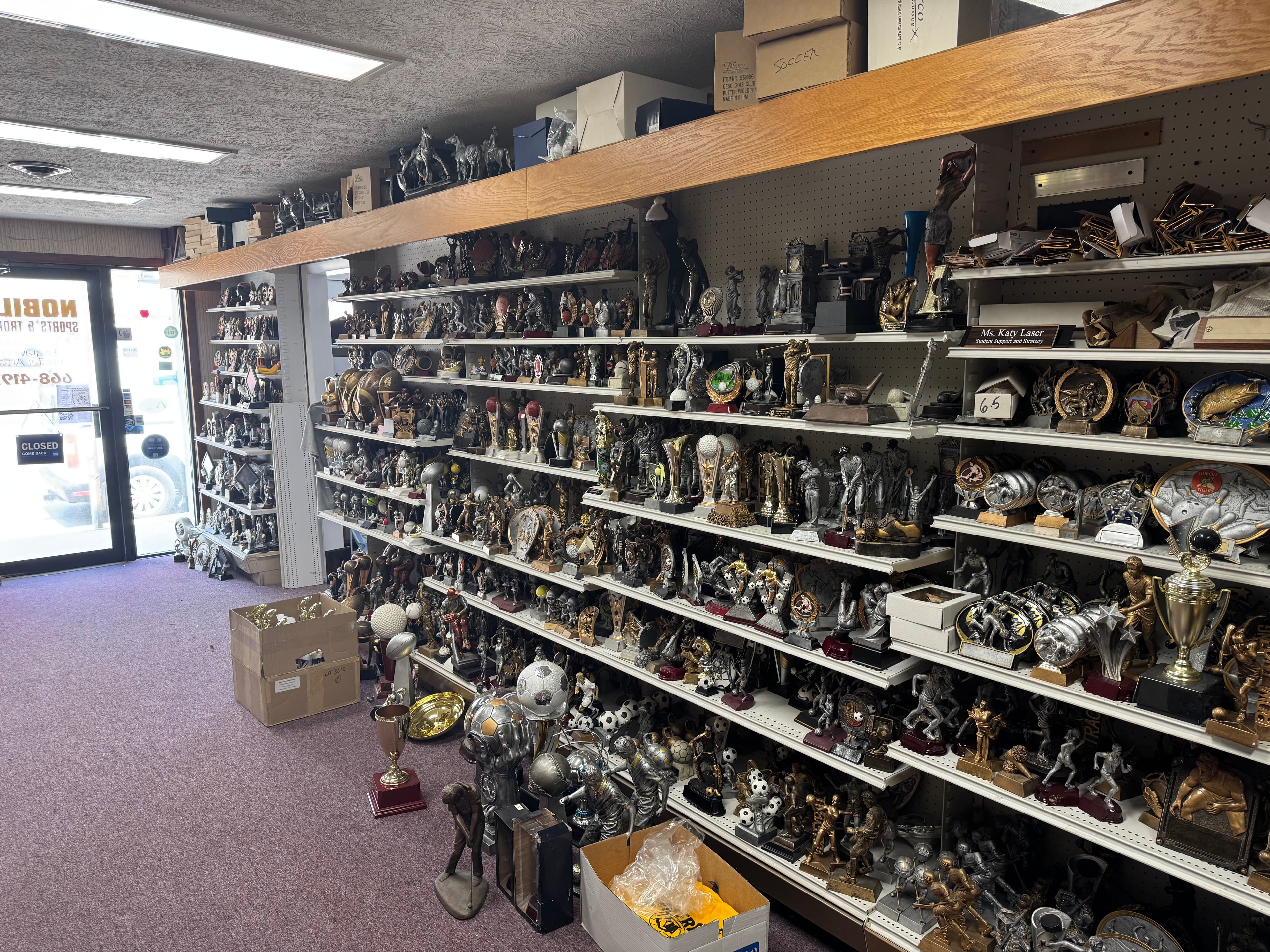 A retail store interior featuring shelves packed with various gold and silver sports trophies.