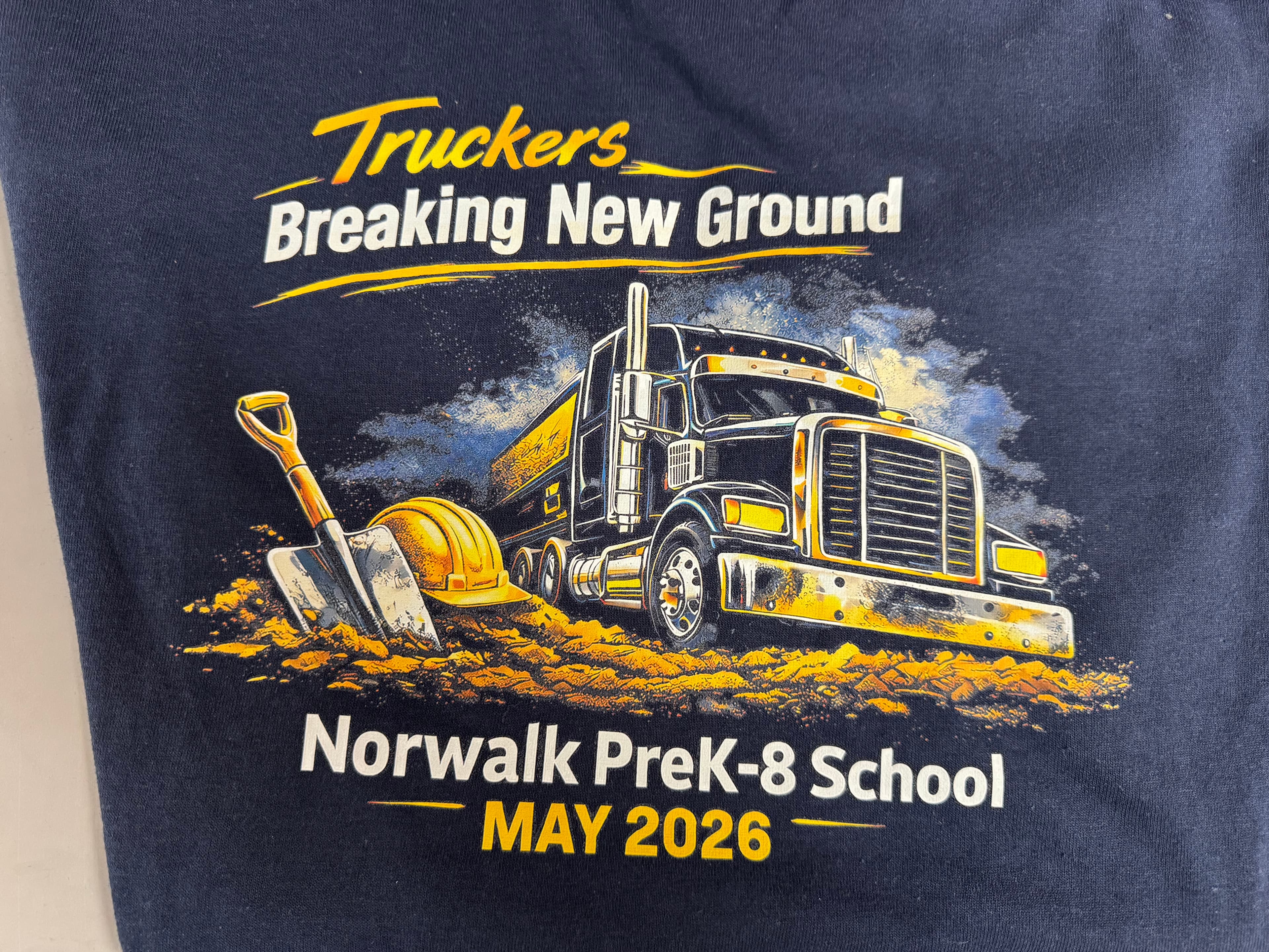 Norwalk PreK-8 School groundbreaking graphic with a semi-truck, hard hat, and shovel, May 2026.