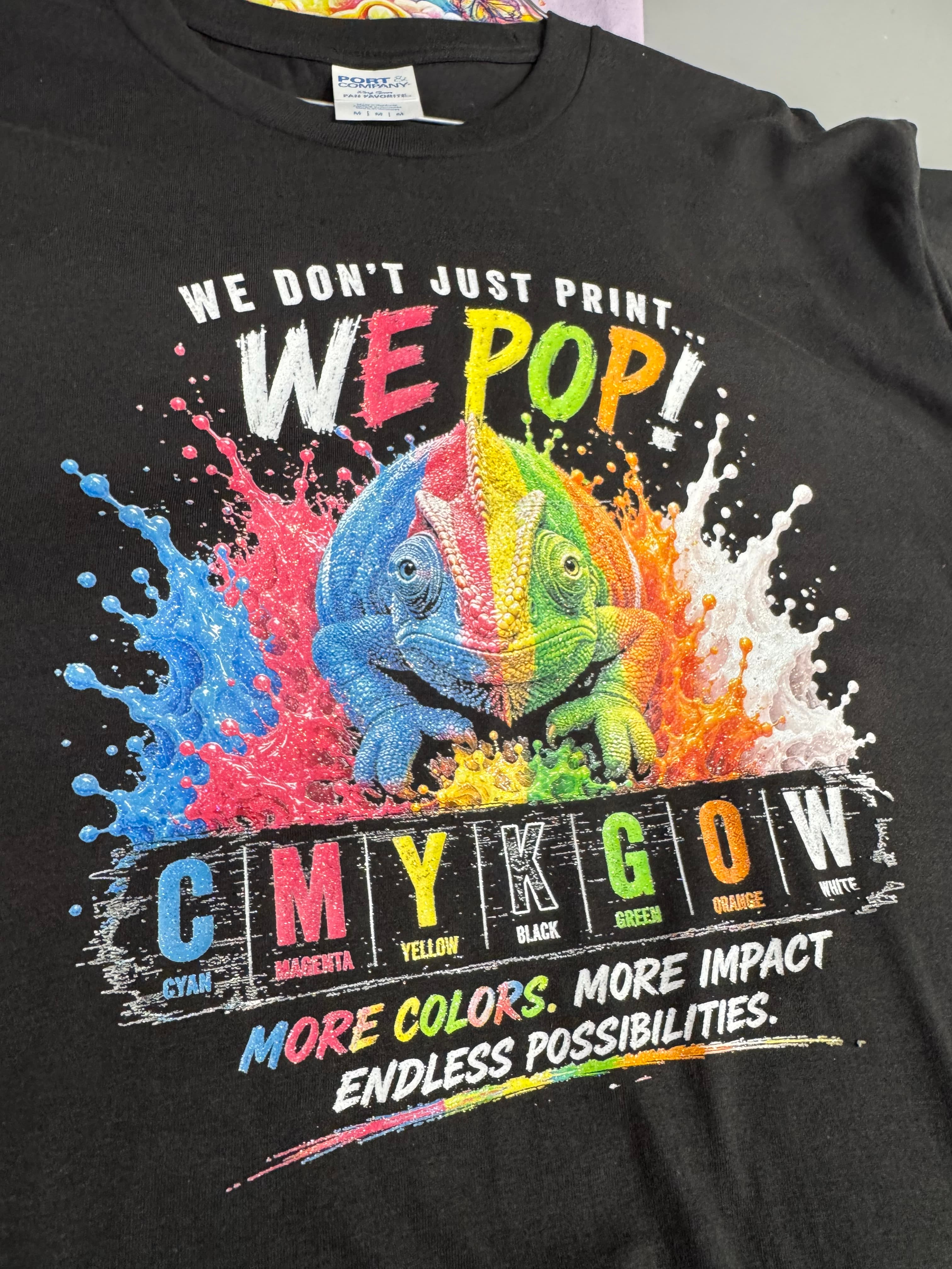 Black t-shirt featuring a vibrant chameleon graphic, colorful paint splashes, and printing-related text.